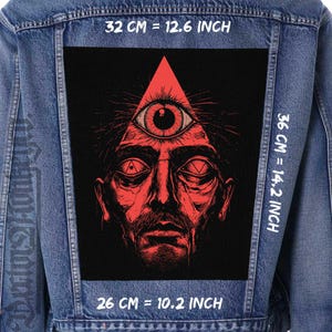 May include: A black and red patch with a stylised image of a face with an all-seeing eye in a triangle. The text "32 CM = 12.6 INCH", "36 CM = 14.2 INCH", and "26 CM = 10.2 INCH" is printed around the patch.