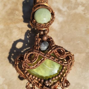 May include: A copper wire wrapped pendant with a green stone and copper beads. The pendant is in the shape of a teardrop.