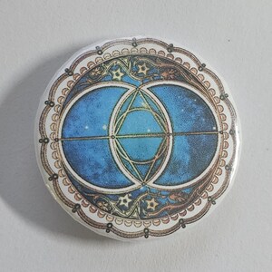 May include: A round button with a blue and gold design. The design features a circle with a star inside, surrounded by a larger circle with a star inside. The design is surrounded by a gold border with a pattern of dots and swirls.