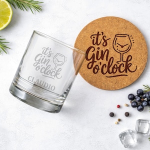 Könnte beinhalten: Ein klares Glas mit der Aufschrift "it's Gin o'clock" und dem Namen "Claudio". Ein runder Untersetzer aus Kork mit dem gleichen Satz und einer Gin-Glas-Illustration liegt neben dem Glas. Garnierungen und Eiswürfel sind verstreut.