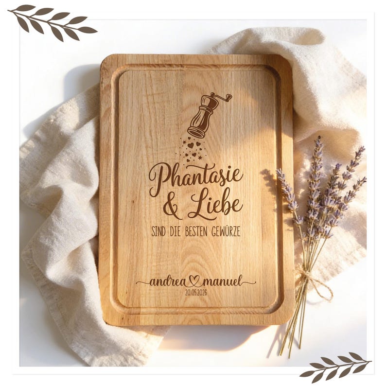 Op de afbeelding: Een rechthoekige houten snijplank met een gesneden rand. De plank heeft de tekst "Phantasie & Liebe sind die besten Gew&uuml;rze" en de namen "andrea & manuel" met een datum. Een pepermolen illustratie staat erboven.
