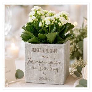 Könnte beinhalten: Ein quadratischer, grauer Beton-Blumentopf mit weißen Blüten und grünen Blättern. Der Topf ist mit den Namen "Andrea & Norbert", einem deutschen Satz, einem Herzen und dem Datum "20.06.2026" beschriftet.