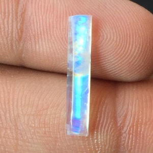 Puede incluir: Una gema rectangular transparente e iridiscente con un brillo azul y morado.