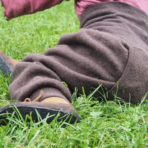 May include: A pair of brown leather shoes with black soles, lying on green grass. The shoes have a brown leather strap across the top.