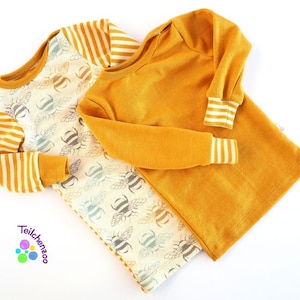 May include: Two long-sleeved shirts, one with a yellow and white striped pattern and the other a solid yellow color. Both shirts have a bee pattern on the front and white cuffs.