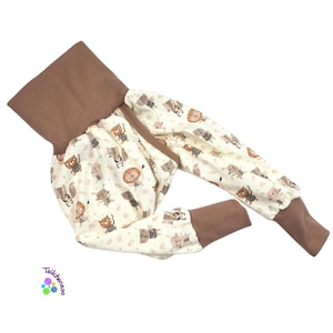 May include: A pair of cream-colored baby pants with a brown waistband and cuffs. The pants have a playful pattern of various animals, including lions, rabbits, and cats.