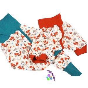 May include: A pair of teal and red baby leggings with a white background and a fox print. The leggings have a gathered elastic waistband.