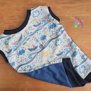 May include: A white sleeveless baby onesie with a blue and yellow nautical print featuring sailboats, waves, fish, and clouds. The onesie has a navy blue trim and a navy blue bottom.
