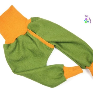 May include: Green and orange baby pants. The pants have an orange waistband and cuffs, with a green body. The pants are made of a soft, textured fabric. The pants are designed for comfort and movement.