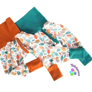 May include: A pair of baby leggings with a white background and a colorful leaf pattern. The leggings have orange and teal cuffs. The leggings are made of soft, comfortable fabric.