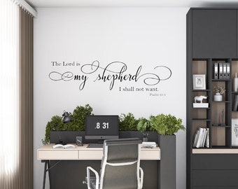 Pode incluir: Um adesivo de parede preto e branco com o texto "The Lord is my shepherd I shall not want. Psalm 23:1" em uma fonte de escrita decorativa. O adesivo é exibido em uma parede branca em um ambiente de escritório em casa.