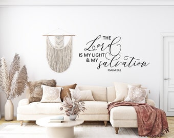 Pode incluir: Um sofá branco com almofadas e uma manta em uma sala de estar. A parede atrás do sofá tem um adesivo de parede preto e branco com o texto "The Lord is my light & my salvation Psalm 27:1".