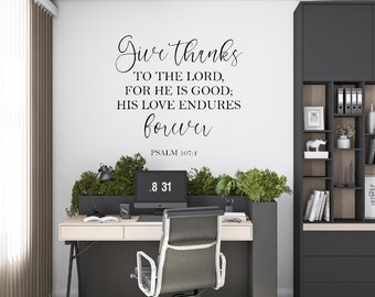 Pode incluir: Um adesivo de parede preto e branco com o texto "Give thanks to the Lord, for he is good; his love endures forever. Psalm 107:1". O adesivo está em uma parede branca em um ambiente de escritório em casa.