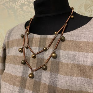 May include: A double-strand necklace made of copper wire with small, round, gold-toned bells hanging from it.