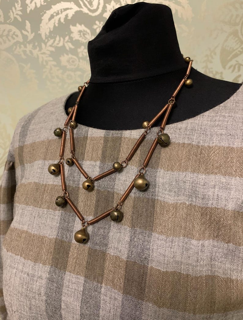 May include: A double-strand necklace made of copper wire with small, round, gold-toned bells hanging from it.