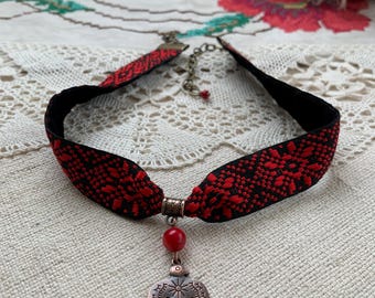 May include: A black choker necklace with a red and black patterned ribbon and a copper bird pendant with a red bead.