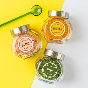 Könnte beinhalten: Drei Glasbehälter mit Etiketten und Deckeln, die verschiedene Gewürze enthalten. Die Behälter befinden sich auf einem gelben und weißen Hintergrund. Die Etiketten lauten "Sel Rose", "Curcuma" und "Persil".