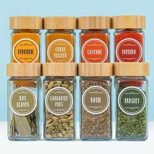 Peut inclure: Huit pots à épices en verre avec des couvercles en bambou, étiquetés avec les noms des épices. Les épices comprennent le curcuma, le curry en poudre, le piment de Cayenne, le paprika, les feuilles de laurier, les gousses de cardamome, le basilic et le persil.