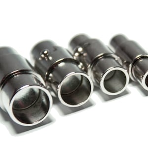 Könnte beinhalten: Vier silberne Metall-Steckverbinder mit einem Gewindedesign. Die Steckverbinder sind in verschiedenen Größen und haben eine glänzende Oberfläche.