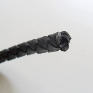 May include: Close-up of a black braided leather cord.