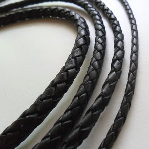 May include: Three black braided leather cords of varying widths. The cords are woven together in a tight, intricate pattern.