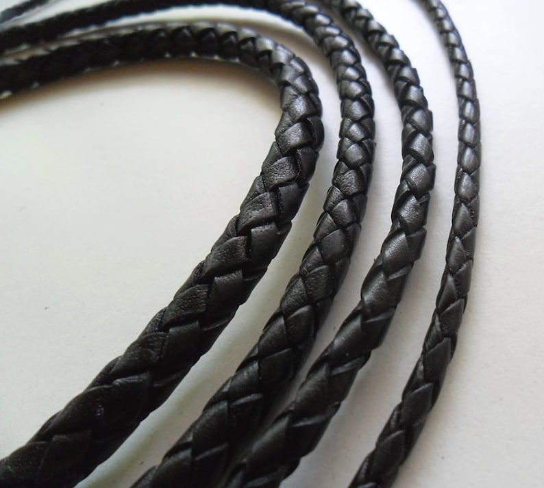 May include: Three black braided leather cords of varying widths. The cords are woven together in a tight, intricate pattern.