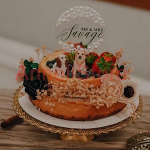 May include: A two-tiered cake topped with two dog figurines, fresh strawberries, and blueberries. A circular acrylic cake topper features a pearl border and the black script text MR & MRS Savage. The cake is decorated with black and cream flowers.