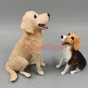 May include: Two dog figurines, one larger light tan dog and one smaller tricolor beagle with black, brown, and white markings. Both dogs are in a sitting position with their mouths slightly open. The text AnneliStore is visible in red.