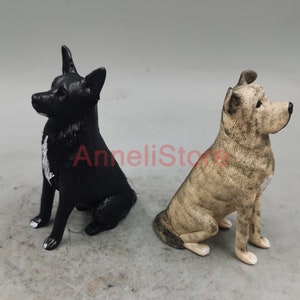 May include: Two dog figurines in a sitting position. One figurine is solid black with a white patch on the chest and white tips on the front paws. The other figurine is tan with dark brown brindle stripes and a white patch on the chest.