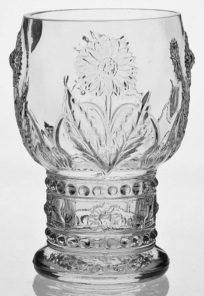 May include: Clear glass goblet with a floral design. The goblet features an embossed flower and leaf pattern, with decorative detailing around the base and stem. The glass has a rounded bowl shape and a sturdy base.