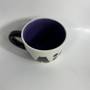 Puede incluir: Una taza de cer&aacute;mica blanca con un asa negra y letras negras que dicen "Wit" en la parte delantera. El interior de la taza es morado.