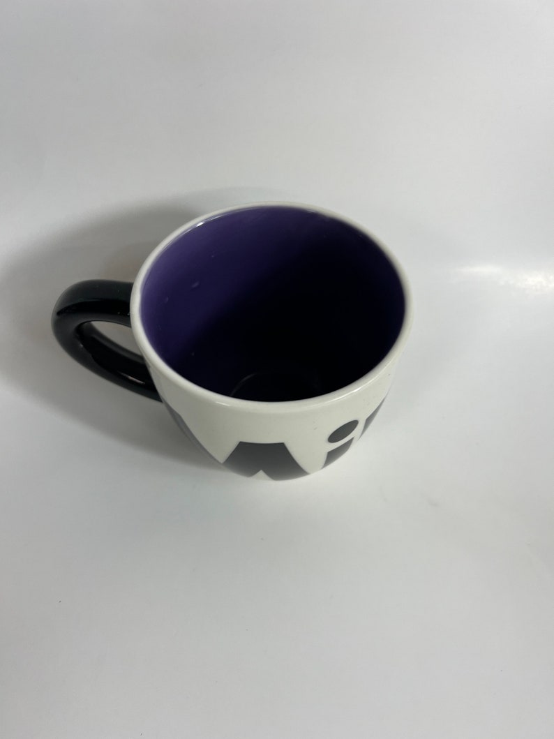 Puede incluir: Una taza de cer&aacute;mica blanca con un asa negra y letras negras que dicen "Wit" en la parte delantera. El interior de la taza es morado.