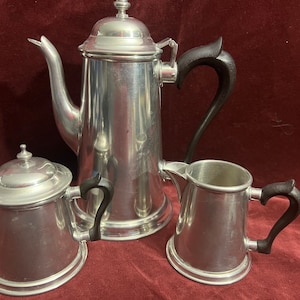 May include: A silver tea set with black handles. The set includes a teapot, creamer, and sugar bowl.