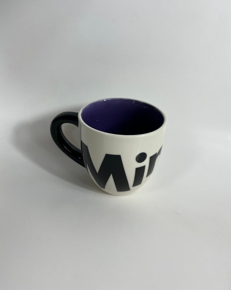 Puede incluir: Taza de cer&aacute;mica blanca con asa negra y la palabra "Mir" en letras negras en la parte delantera. El interior de la taza es morado.