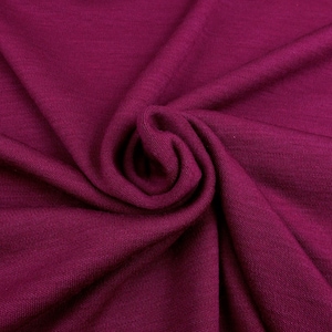 Könnte beinhalten: Nahaufnahme eines tiefmagentafarbenen Stoffes mit weicher Textur. Das Material ist gerafft und gewirbelt, wodurch ein Spiraleffekt in der Mitte entsteht. Der Stoff scheint ein Strick- oder Webtextil zu sein.
