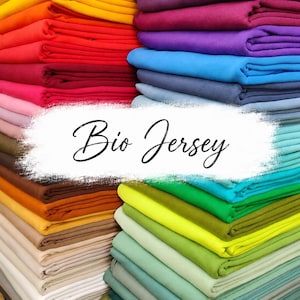 Könnte beinhalten: Stapel bunter Stoffe in Gelb-, Orange-, Rot-, Rosa-, Braun-, Beige-, Lila-, Blau-, Grün- und Türkistönen. Der Text "Bio Jersey" ist in Kursivschrift über das Bild geschrieben.