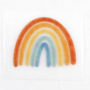 Könnte beinhalten: Ein farbenfrohes Regenbogen-Design mit orangefarbenen, gelben, grünen und blauen Bögen auf weißem Hintergrund. Das Design ist wahrscheinlich für Bastel- oder Dekorationszwecke gedacht.