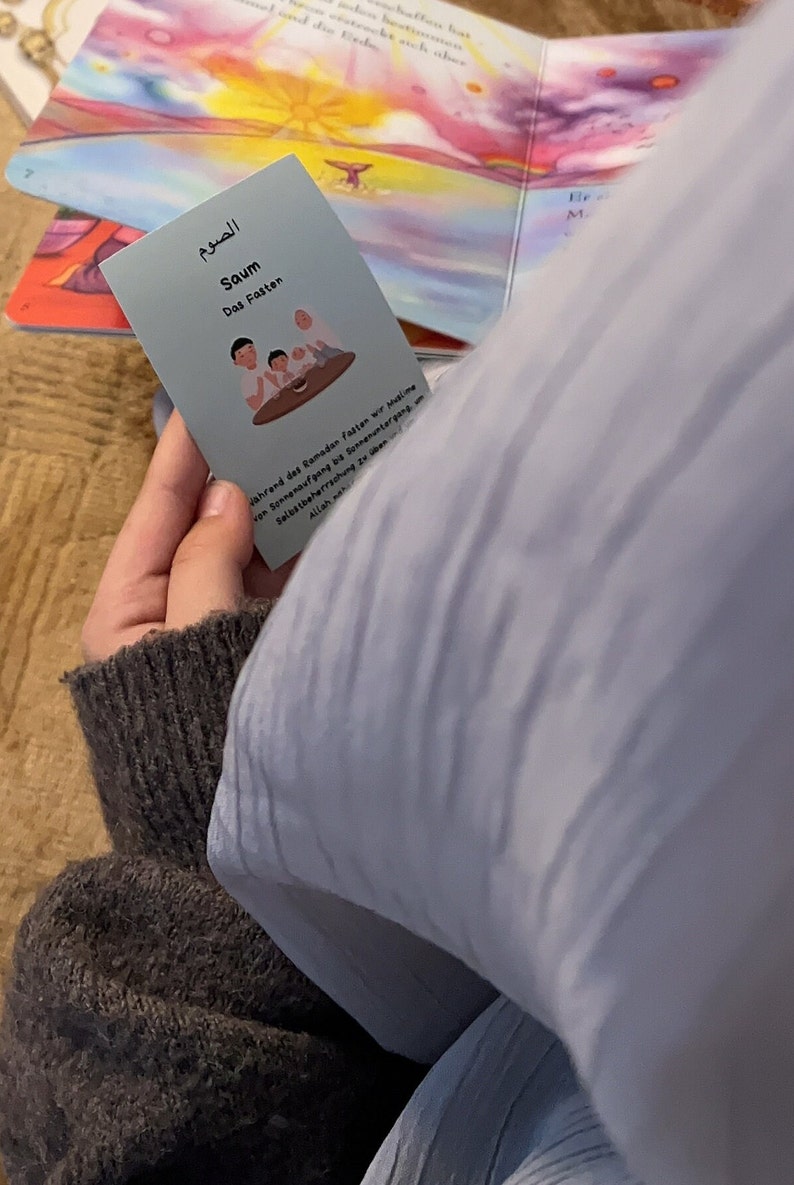May include: A blue card with Arabic text and the word "Saum" which means "Fasting" in English. The card also has an illustration of three people sitting at a table. The text on the card reads: "During Ramadan, Muslims fast from sunrise to sunset. Self-discipline in obedience to Allah."
