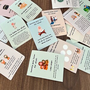 May include: A set of colorful cards with Islamic teachings and illustrations. The cards feature phrases in Arabic and German, such as "La ilaha illa Allah" and "Sammle gute Taten f&uuml;r Allah!" The cards are designed for children and feature illustrations of people praying, giving charity, and learning the Quran.