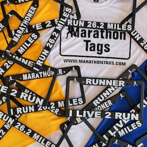 May include: A collection of black license plate frames and athletic shirts. The frames have white text that reads "MARATHONER", "RUNNER", and "I RUN 26.2 MILES". Shirts are yellow, white, and blue, with "Marathon Tags" printed on them.