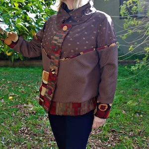 May include: A brown jacket with a geometric pattern on the sleeves and a high collar. The jacket is made of a textured fabric and has a button closure.