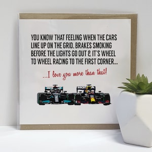 May include: A greeting card with a white background and a message about the feeling of cars lining up on the grid before a race. The card features a photo of two Formula 1 race cars. The text on the card reads: "YOU KNOW THAT FEELING WHEN THE CARS LINE UP ON THE GRID, BRAKES SMOKING BEFORE THE LIGHTS GO OUT & IT'S WHEEL TO WHEEL RACING TO THE FIRST CORNER... ...I love you more than that!"