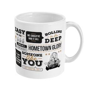 May include: White ceramic mug with a black and gold design featuring lyrics from the song "Someone Like You" by Adele. The lyrics include "Easy on Me", "Rolling in the Deep", "Hometown Glory", and "Don't Forget Me, I Beg".