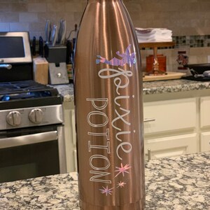 May include: A copper-colored stainless steel water bottle with a white design that says "Pixie Potion" with a fairy graphic and stars.