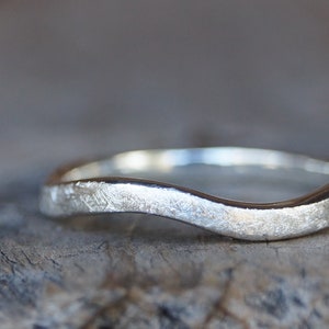 Könnte beinhalten: Ein silberner Wellenring mit strukturierter Oberfläche. Der Ring ist aus Sterlingsilber gefertigt und hat ein schlichtes, aber elegantes Design.