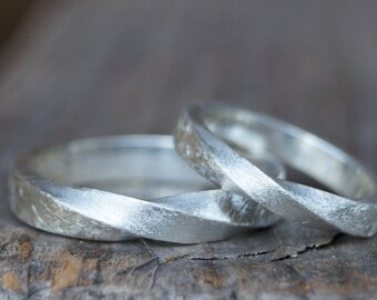 May include: Two silver rings with a textured, twisted design. The rings are close together, showcasing their unique shape and metallic sheen. The rings are likely for a wedding or engagement.
