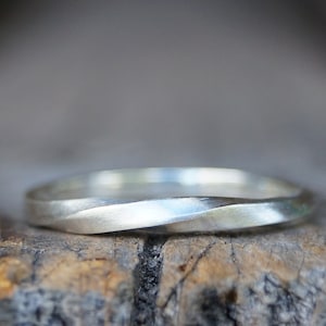 Könnte beinhalten: Ein silberfarbener Ring mit einem gedrehten Design. Der Ring hat eine glatte, polierte Oberfläche und einen schlichten, eleganten Stil. Der Ring ist wahrscheinlich aus Sterlingsilber oder einem ähnlichen Metall gefertigt.