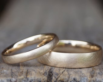 May include: Two gold wedding bands with a brushed finish. The bands are stacked on top of each other.