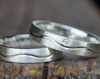 May include: Two silver wedding bands with a wavy design and a small diamond on one band.