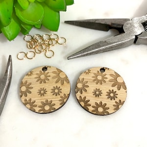 May include: Two round wooden earrings with a laser-cut design of small brown flowers on a light brown background.